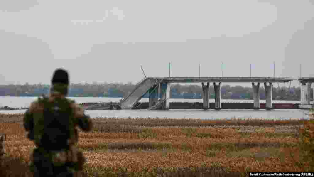 A Ukrainian soldier looks at the destroyed Antonivskiy Bridge, in the east of Kherson. The crucial bridge had been out of action for much of the Russian occupation as Ukraine targeted one end of the span with repeated rocket strikes -- reportedly using U.S.-made HIMARS systems. As Russian forces retreated on November 11, a large explosion led to the collapse of the bridge.