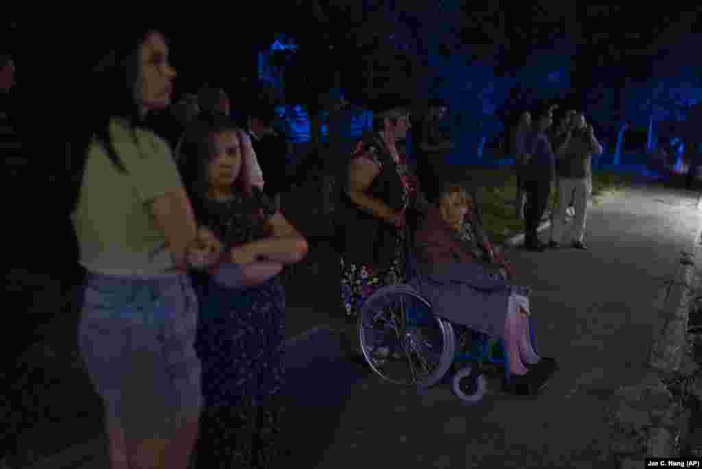 Residents stand outside a damaged apartment building as rescuers and emergency personnel survey the damage.