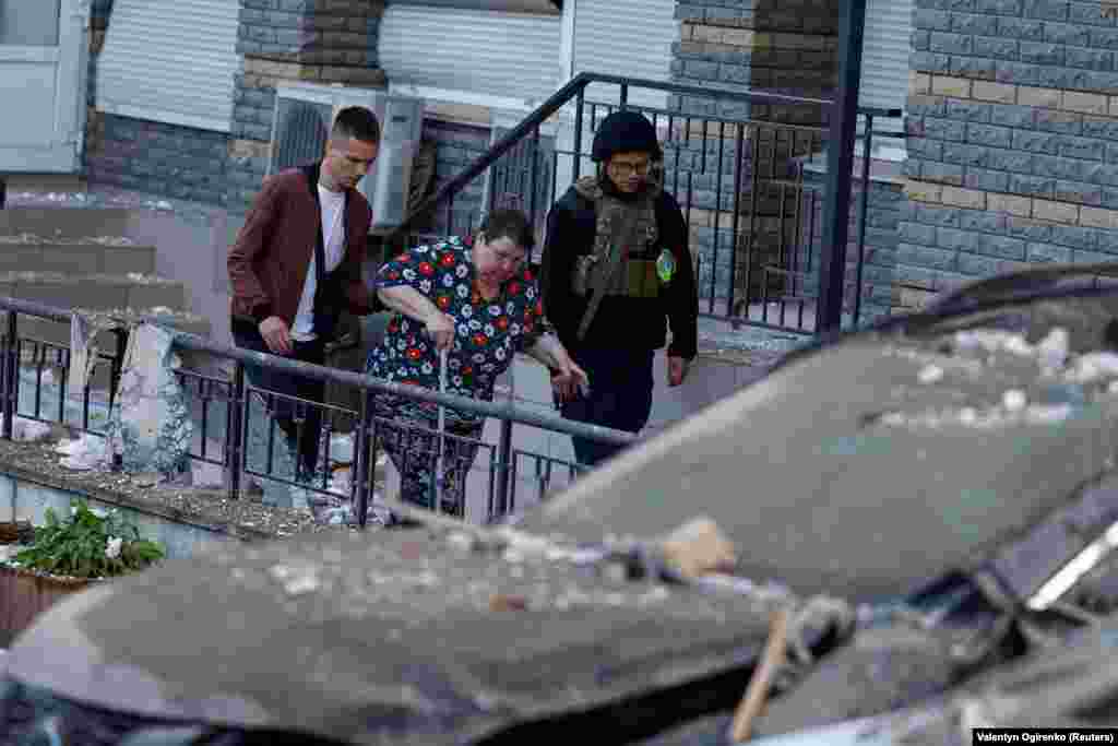 Men assist a woman as she leaves her damaged apartment building.