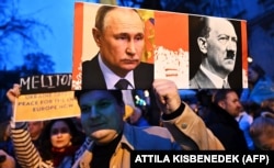 Плакат із зображенням керівника РФ Володимира Путіна й Адольфа Гітлера на акції біля посольства РФ в Угорщині. Будапешт, 24 лютого 2024 року