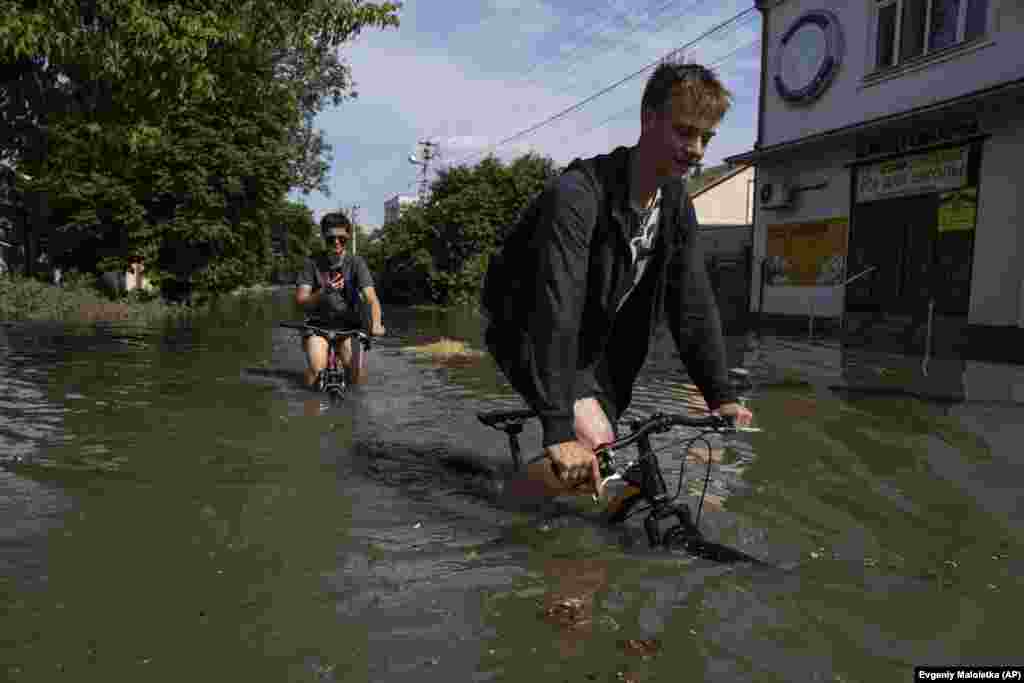 Local residents try to ride their bikes along a flooded road in Kherson. 
