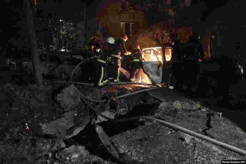 Emergency workers extinguish a fire in a parked car caused by falling debris from the Russian drone strike in the Pecherskiy district of Kyiv.