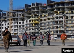 Workers walk in front of an apartment building under construction in Mariupol in Russian-occupied Ukraine in February 2023.