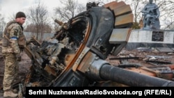 Український військовослужбовець оглядає залишки знищеного російського танка у селі Лук'янівка Київської області. Саме війна Росії проти України підштовхує нордичні Фінляндію та Швецію до можливого членства в НАТО, кажуть політики цих країн