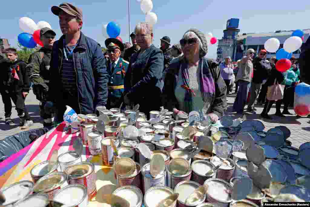 People wait next to a table with open tins of canned meat.