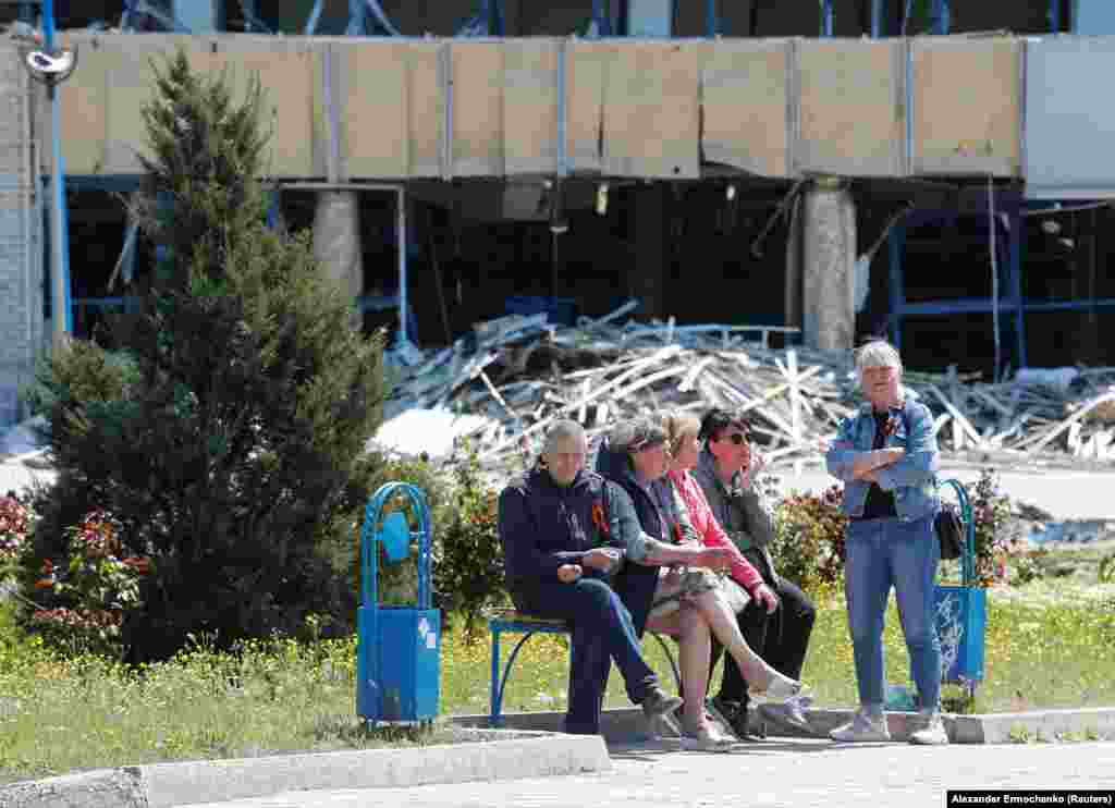 Mariupol residents wearily watch the celebration from across the street.