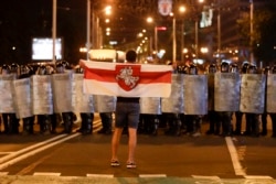 Учасник протесту тримає біло-червоно-білий прапор перед поліцією під час мітингу після білоруських президентських виборів у Мінську, 9 серпня 2020 року