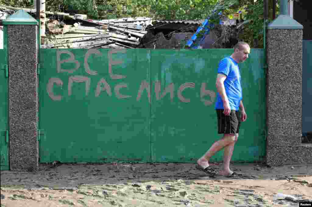 A local resident walks in mud from the floods in the town of Krymsk past a sign reading&nbsp;&nbsp;&quot;Everyone has escaped (found salvation).&quot;