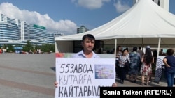 Асқар Қайырбек "55 зауыт Қытайға қайтарылсын!" деген жазуы бар плакат ұстап, Бəйтерек монументі алдында бір адамдық пикет жасап тұр. Нұр-Сұлтан, 18 тамыз 2019 жыл.