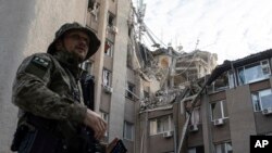 Херсонго урулган орус аба соккусунан катуу жабыркаган имараттын жанында турган украин аскери. Украина. 15-июнь, 2023-жыл. AP Photo/Евгений Малолетка.