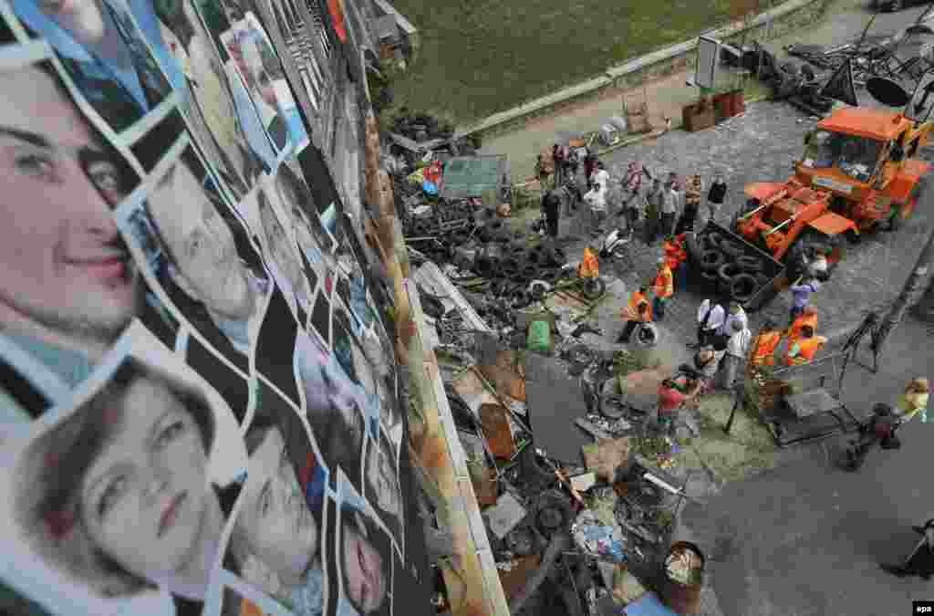 Pictures of people who were killed during the winter protests are attached to a bridge as municipal workers clean up a barricade on Independence Square in Kyiv on August 11, 2014. The downtown area of the Ukrainian capital was reopened after citizens had cleaned up the central streets two days previously.