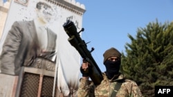 Боевик антиправительственного движения стоит у изуродованного портрета президента Сирии Башара Асада. Город Хама, 6 декабря 2024 года