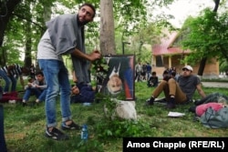 A young man places a flower onto an upside-down portrait of Prime Minister Serzh Sarkisian in a children’s park in Yerevan. The frame features a black strip of cloth at the corner, traditionally placed over a portrait when someone is dead.