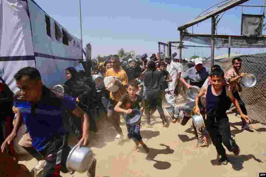 Palestinieni se grăbesc să ajungă la coadă la o cantină socială din zona Mawasi din Khan Yunis, în sudul Fâșiei Gaza. 22 iulie 2025.Potrivit ONU, aproximativ 900.000 de copii din Gaza suferă de foame, iar 70.000 dintre ei sunt în stare de malnutriție