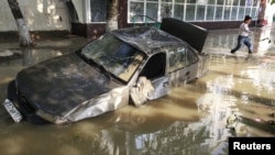 A local resident passes by a damaged car stuck in a flooded street in the town of Krymsk in the Krasnodar region on July 8.